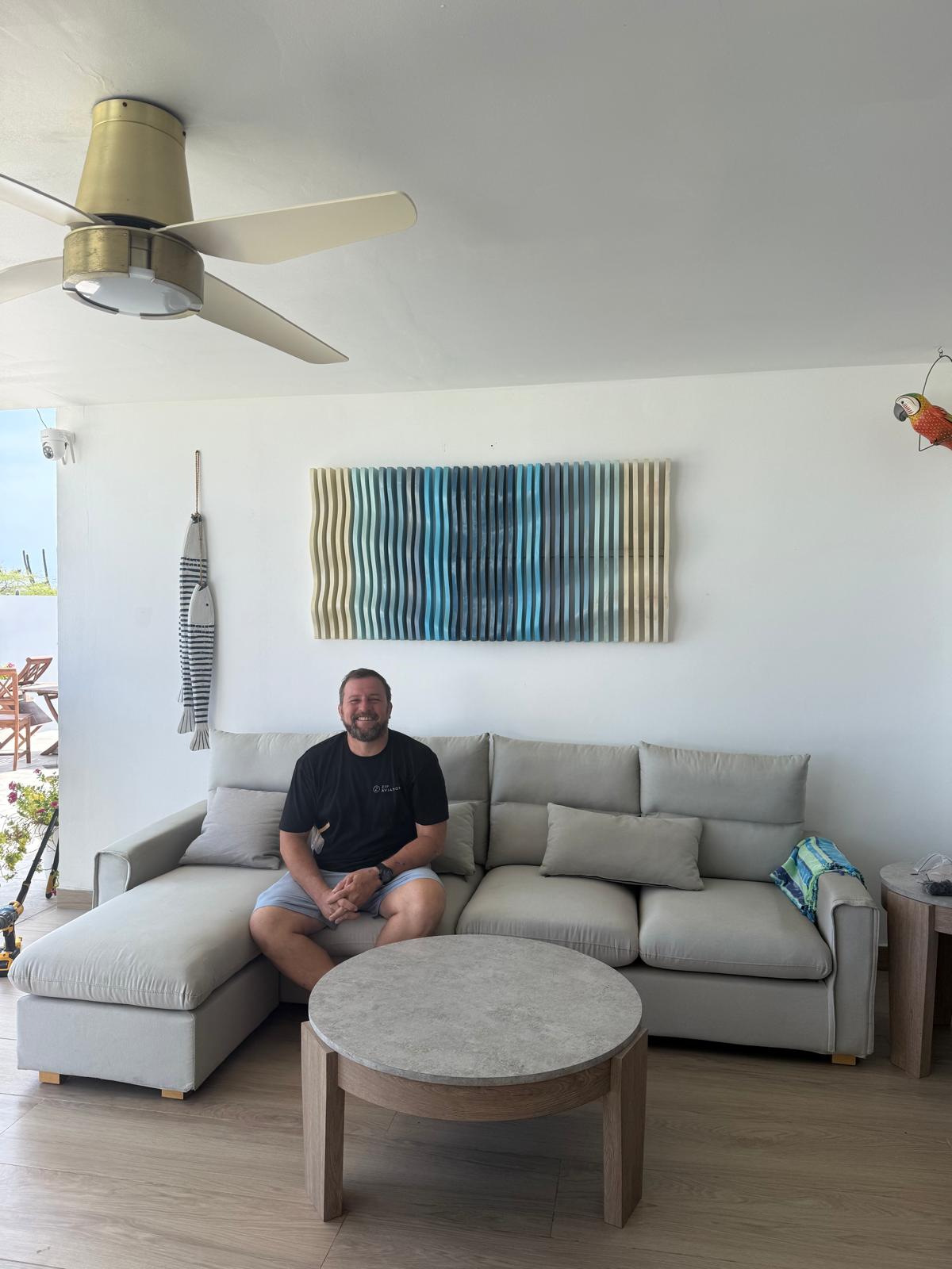 Juan seated beneath one of his blue and cream wood reliefs.
